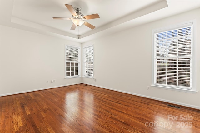 unfurnished room with baseboards, ceiling fan, a tray ceiling, and wood finished floors