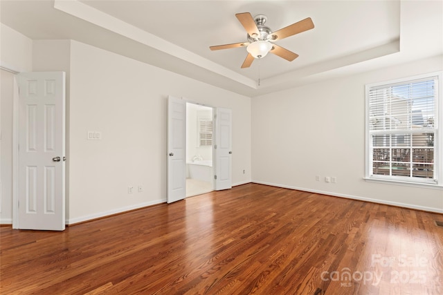 unfurnished bedroom with wood finished floors, a raised ceiling, connected bathroom, and baseboards