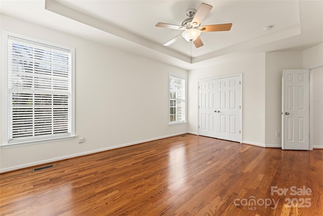 unfurnished bedroom featuring a tray ceiling, visible vents, baseboards, and wood finished floors