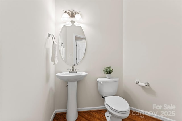 half bath featuring toilet, baseboards, a sink, and wood finished floors