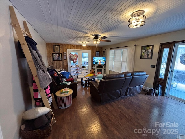 living area featuring a warm lit fireplace, wooden ceiling, and wood finished floors