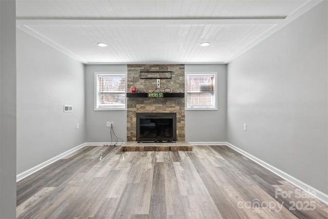 unfurnished living room featuring a stone fireplace, plenty of natural light, wood finished floors, and baseboards