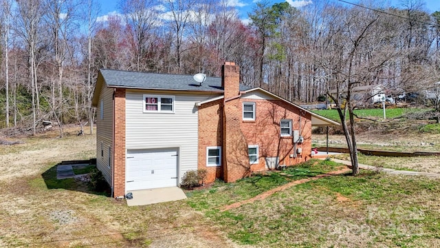 view of side of property with a garage, brick siding, a chimney, and a lawn