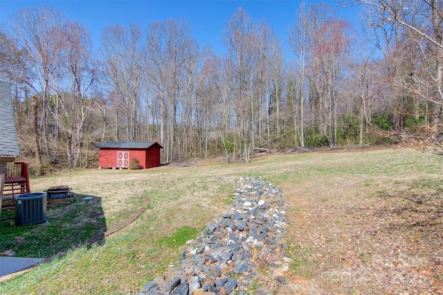 view of yard featuring a wooded view, a shed, an outdoor structure, and cooling unit