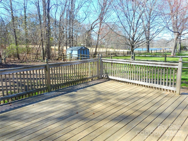 wooden terrace with a water view, fence, a storage unit, and an outbuilding