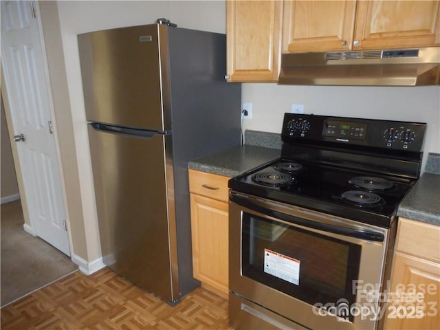 kitchen featuring stainless steel appliances, dark countertops, light brown cabinetry, under cabinet range hood, and baseboards