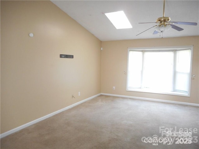 carpeted spare room with ceiling fan, vaulted ceiling with skylight, and baseboards