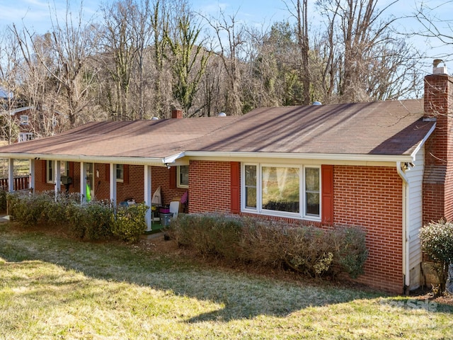 single story home featuring a porch, a front yard, brick siding, and a chimney