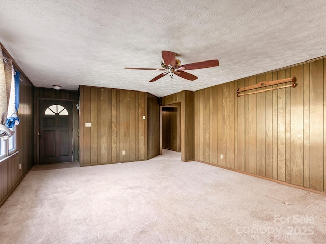 spare room with a textured ceiling, wood walls, carpet flooring, a ceiling fan, and baseboards