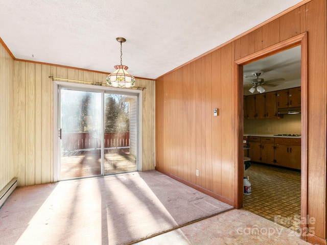 unfurnished dining area with crown molding, baseboard heating, carpet flooring, ceiling fan, and wooden walls