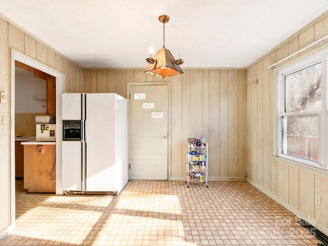 kitchen featuring wood walls, white refrigerator with ice dispenser, baseboards, and tile patterned floors