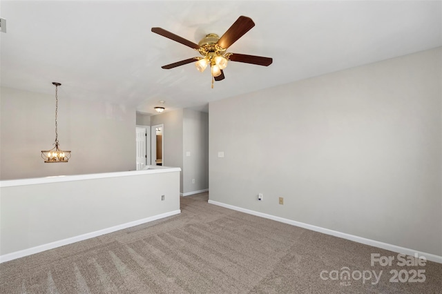 carpeted spare room featuring ceiling fan with notable chandelier, visible vents, and baseboards