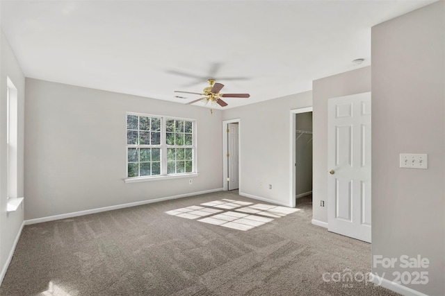 unfurnished bedroom featuring a spacious closet, baseboards, carpet, a closet, and a ceiling fan