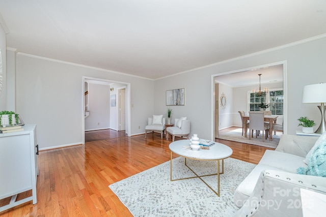 living area with baseboards, ornamental molding, light wood-type flooring, and a notable chandelier