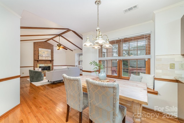 dining room with vaulted ceiling with beams, light wood finished floors, visible vents, a brick fireplace, and ceiling fan with notable chandelier