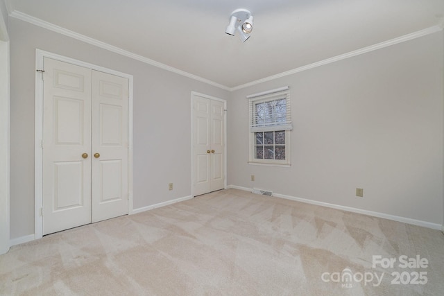 unfurnished bedroom featuring baseboards, visible vents, ornamental molding, carpet flooring, and two closets