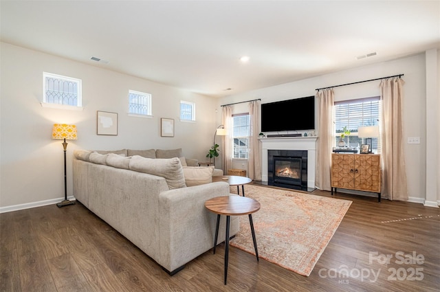 living area featuring baseboards, visible vents, dark wood finished floors, and a glass covered fireplace