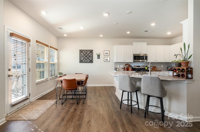 kitchen with dark wood-style flooring, white cabinets, a kitchen breakfast bar, appliances with stainless steel finishes, and backsplash