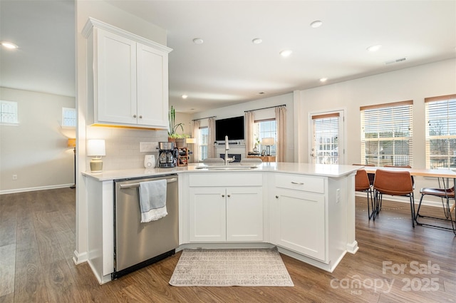 kitchen featuring light countertops, white cabinetry, a sink, dishwasher, and a peninsula