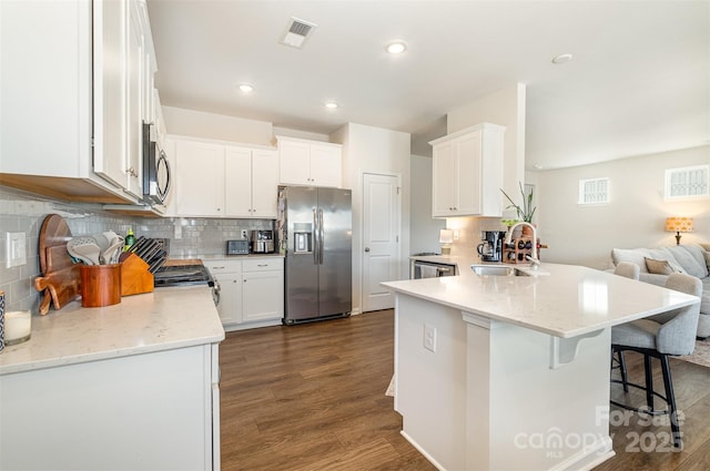 kitchen with stainless steel appliances, a peninsula, dark wood-style flooring, a sink, and visible vents