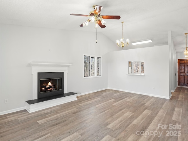 unfurnished living room featuring vaulted ceiling, a lit fireplace, baseboards, and wood finished floors