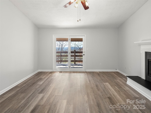 unfurnished living room featuring a textured ceiling, baseboards, wood finished floors, and a glass covered fireplace