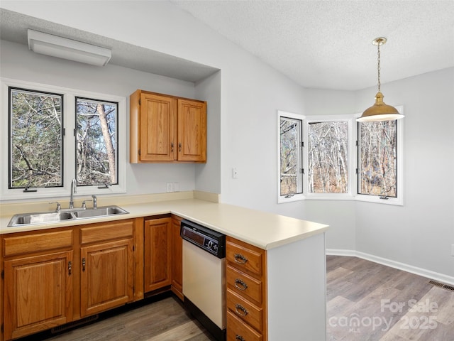 kitchen with visible vents, wood finished floors, a peninsula, white dishwasher, and a sink