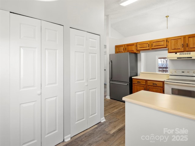 kitchen with under cabinet range hood, white electric range, vaulted ceiling, freestanding refrigerator, and brown cabinetry