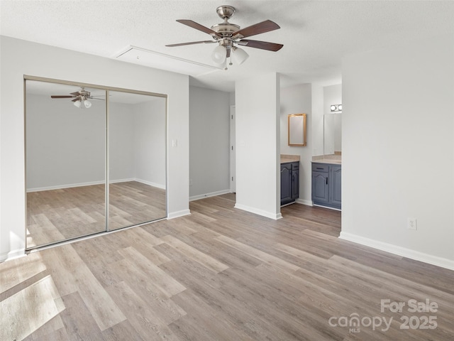 unfurnished bedroom with light wood finished floors, a closet, attic access, a textured ceiling, and baseboards