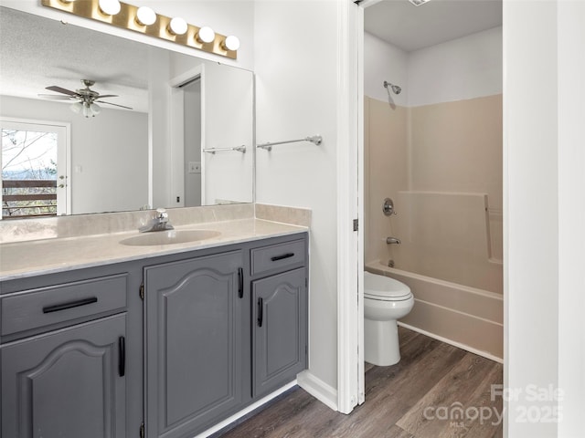 full bath with a ceiling fan, toilet, vanity, wood finished floors, and shower / bathtub combination