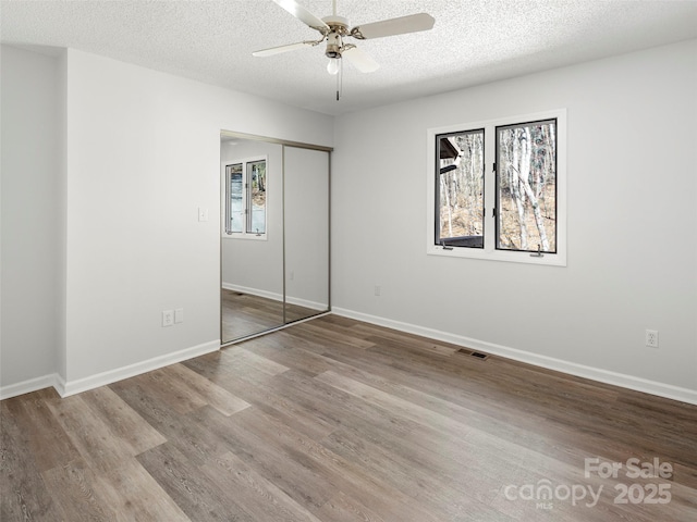 unfurnished bedroom featuring a closet, visible vents, a textured ceiling, wood finished floors, and baseboards