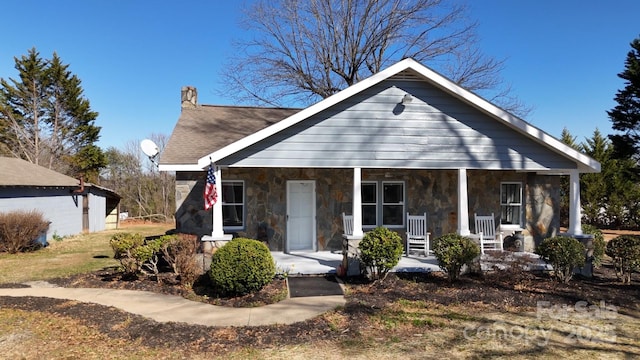 bungalow-style house with a porch, stone siding, and a chimney