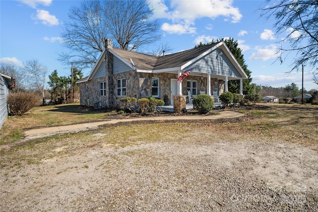 view of front of property featuring stone siding, covered porch, a chimney, and central air condition unit