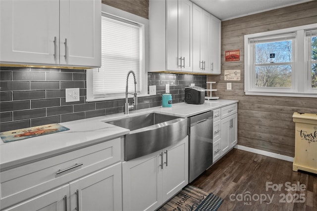 kitchen with dark wood-type flooring, stainless steel dishwasher, wood walls, and a sink