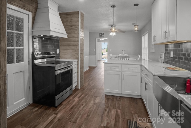 kitchen with dark wood-type flooring, a peninsula, stainless steel range with electric cooktop, premium range hood, and white cabinetry