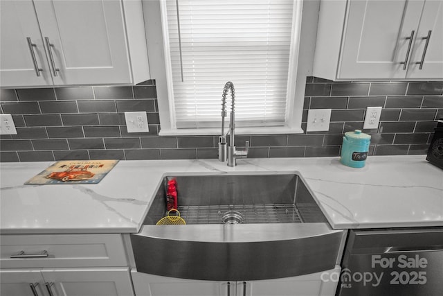 kitchen featuring stainless steel dishwasher, white cabinets, light stone counters, and decorative backsplash