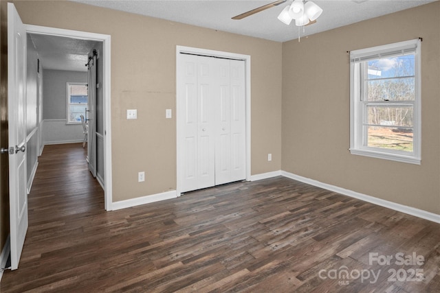 unfurnished bedroom with ceiling fan, dark wood-type flooring, a closet, and baseboards