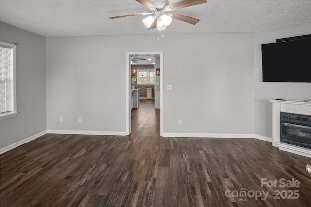 unfurnished living room featuring a ceiling fan, a glass covered fireplace, a textured ceiling, wood finished floors, and baseboards