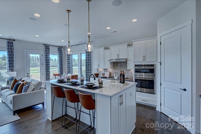 kitchen with tasteful backsplash, white cabinets, double oven, and dark wood finished floors