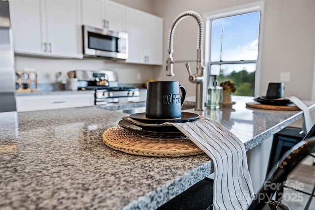 kitchen featuring stainless steel appliances, a breakfast bar, white cabinetry, and light stone counters