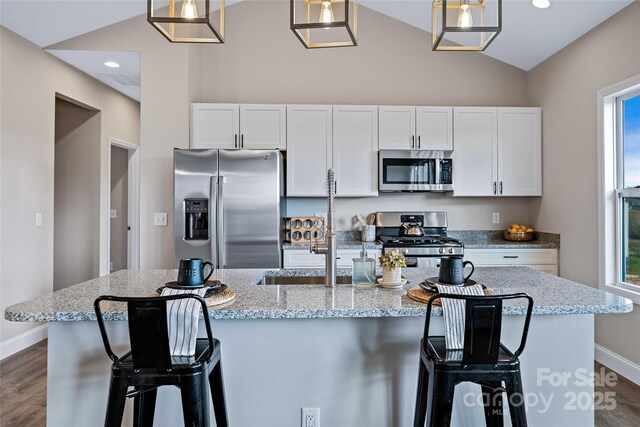 kitchen with lofted ceiling, stainless steel appliances, dark wood-style flooring, white cabinets, and a center island with sink