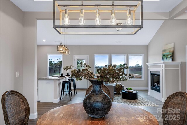 living room featuring lofted ceiling, baseboards, wood finished floors, and a glass covered fireplace