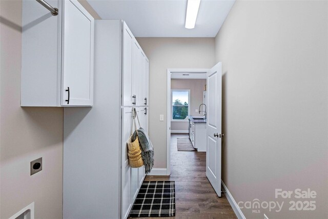 clothes washing area featuring cabinet space, baseboards, dark wood finished floors, hookup for an electric dryer, and a sink