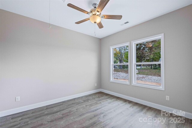 unfurnished room with a ceiling fan, wood finished floors, visible vents, and baseboards