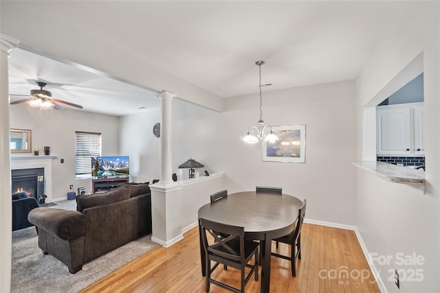 dining room with a warm lit fireplace, decorative columns, light wood-style flooring, and baseboards