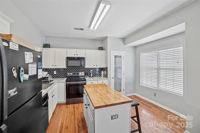 kitchen with black appliances, a kitchen bar, white cabinetry, and wooden counters