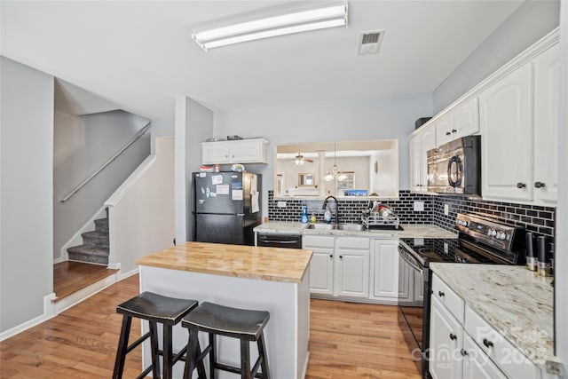 kitchen with a breakfast bar, visible vents, electric range oven, freestanding refrigerator, and a sink