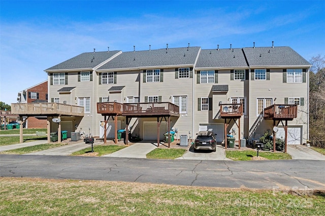 rear view of property featuring central AC, concrete driveway, an attached garage, and a wooden deck