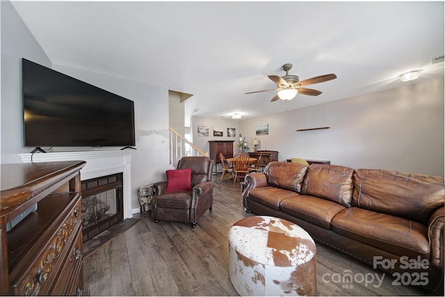 living room with visible vents, a ceiling fan, wood finished floors, a fireplace, and stairs