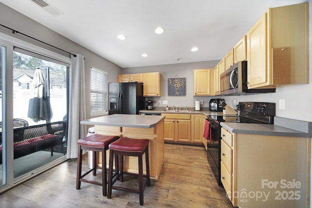 kitchen with light brown cabinets, light wood-style flooring, a sink, black appliances, and a kitchen bar